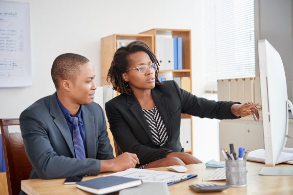 Pretty business woman showing information on computer screen to coworker